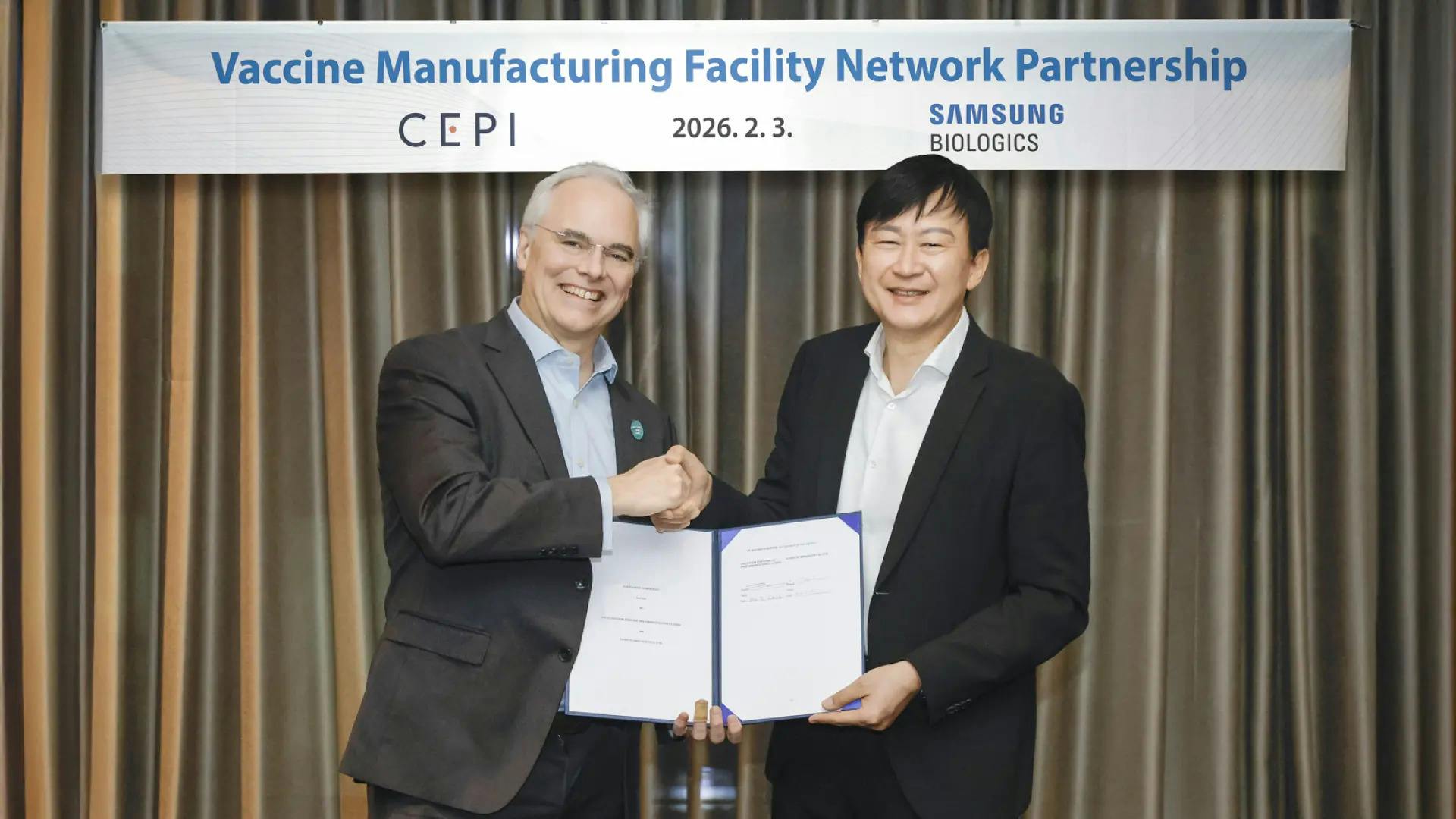 CEPI&rsquo;s Vaccine Manufacturing Facility Network (VMFN) partnership banner in background with two execs from CEPI and Samsung Biologics shaking hands on their new partnership