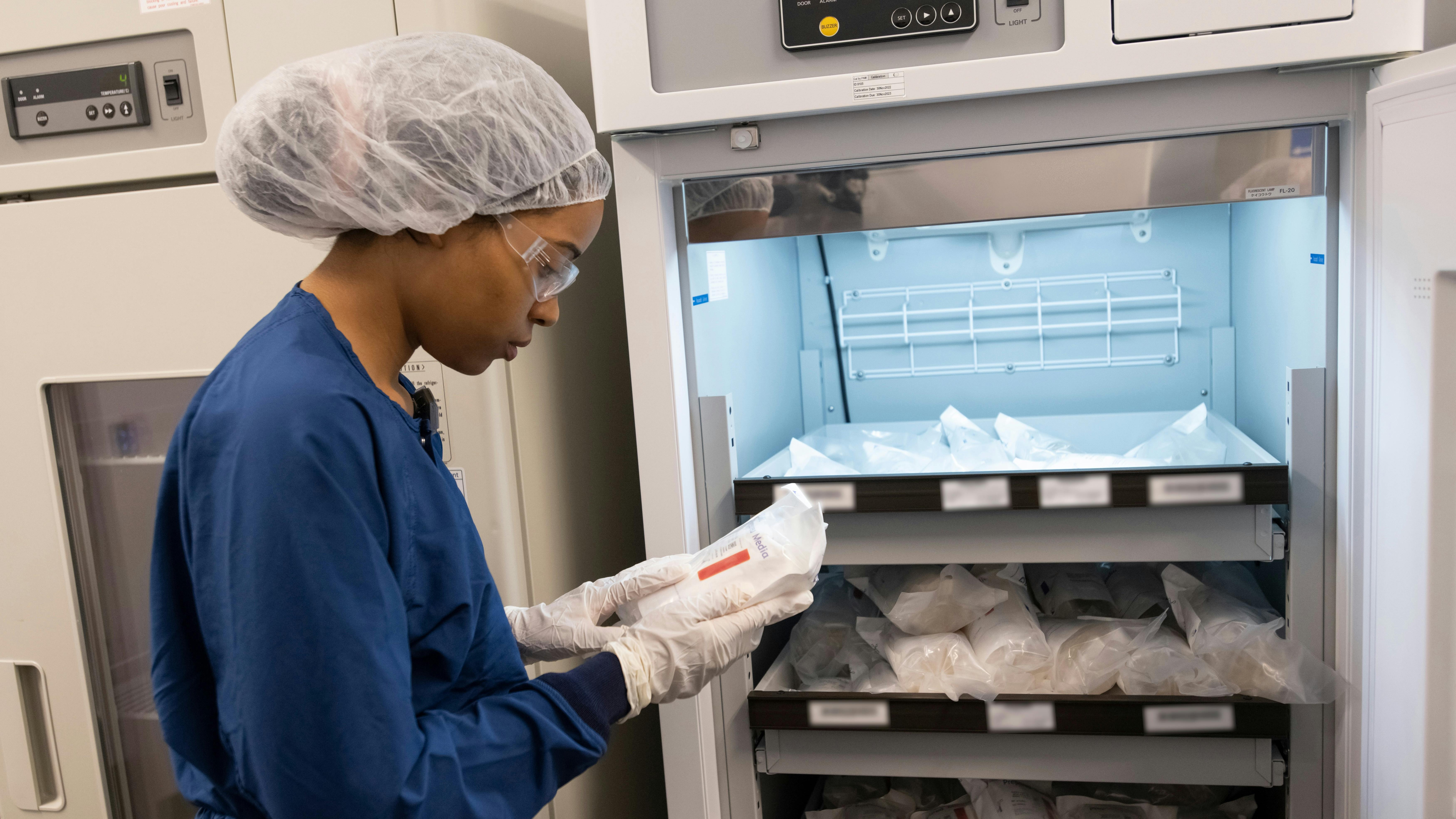 a female worker in personal protective equipment examines materials inside the refrigeration room of Novartis radioligand therapy (RLT) manufacturing facility