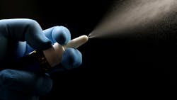 A gloved hand holding a nasal spray bottle, actively dispensing a fine mist spray against a black background. A gloved hand holding a nasal spray bottle, actively dispensing a fine mist spray against a black background.