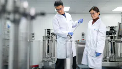 Two Ecolab scientists in white lab coats and blue gloves examine equipment in a modern laboratory. Two Ecolab scientists in white lab coats and blue gloves examine equipment in a modern laboratory.