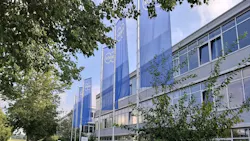 Körber flags fly in front of corporate building surrounded by trees in foreground Körber flags fly in front of corporate building surrounded by trees in foreground