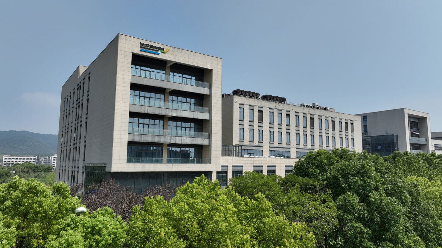 Exterior view of WuXi Biologics' Suzhou Biosafety Testing Center building rising above treeline