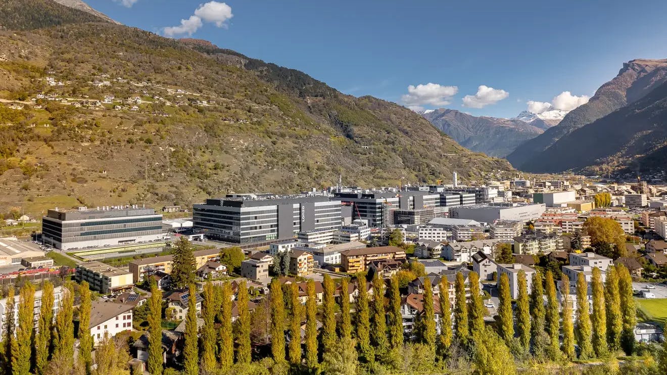 Aerial view overlooking several buildings that make up the Lonza site in Visp, Switzerland. Mountains in the background