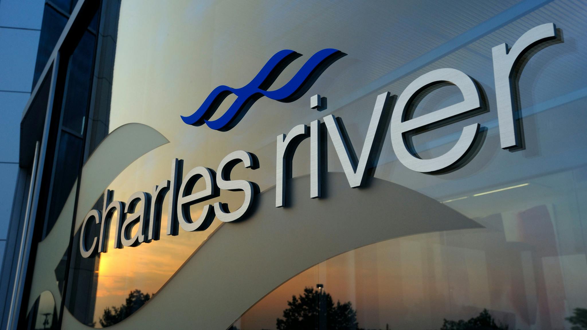Close up view of Charles River logo on glass building that reflects sky at dusk