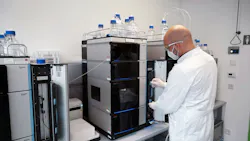 A lab scientist at Leukocare in a white coat wearing a mask operates a Thermo Scientific Vanquish HPLC system.