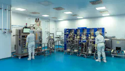 Two cleanroom-suited technicians operate bioreactor equipment in Enzene's biomanufacturing facility.