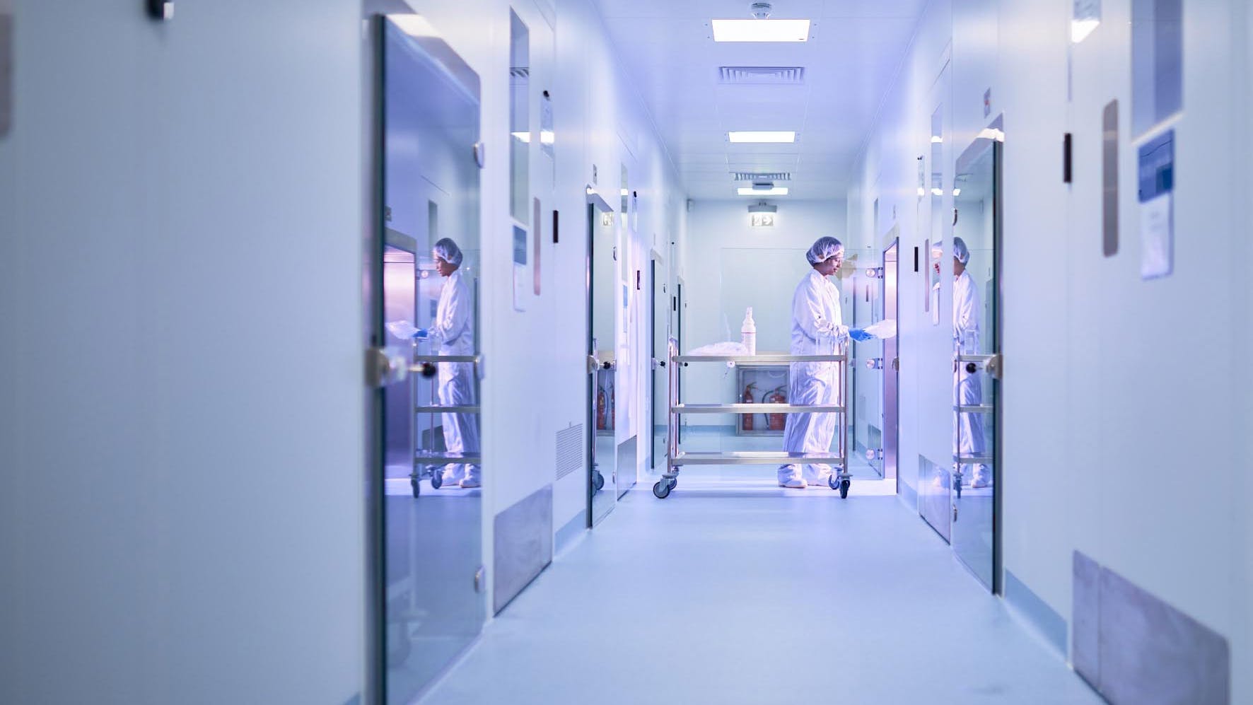 Image of hallway where worker in PPE pushes cart into lab at Touchlight