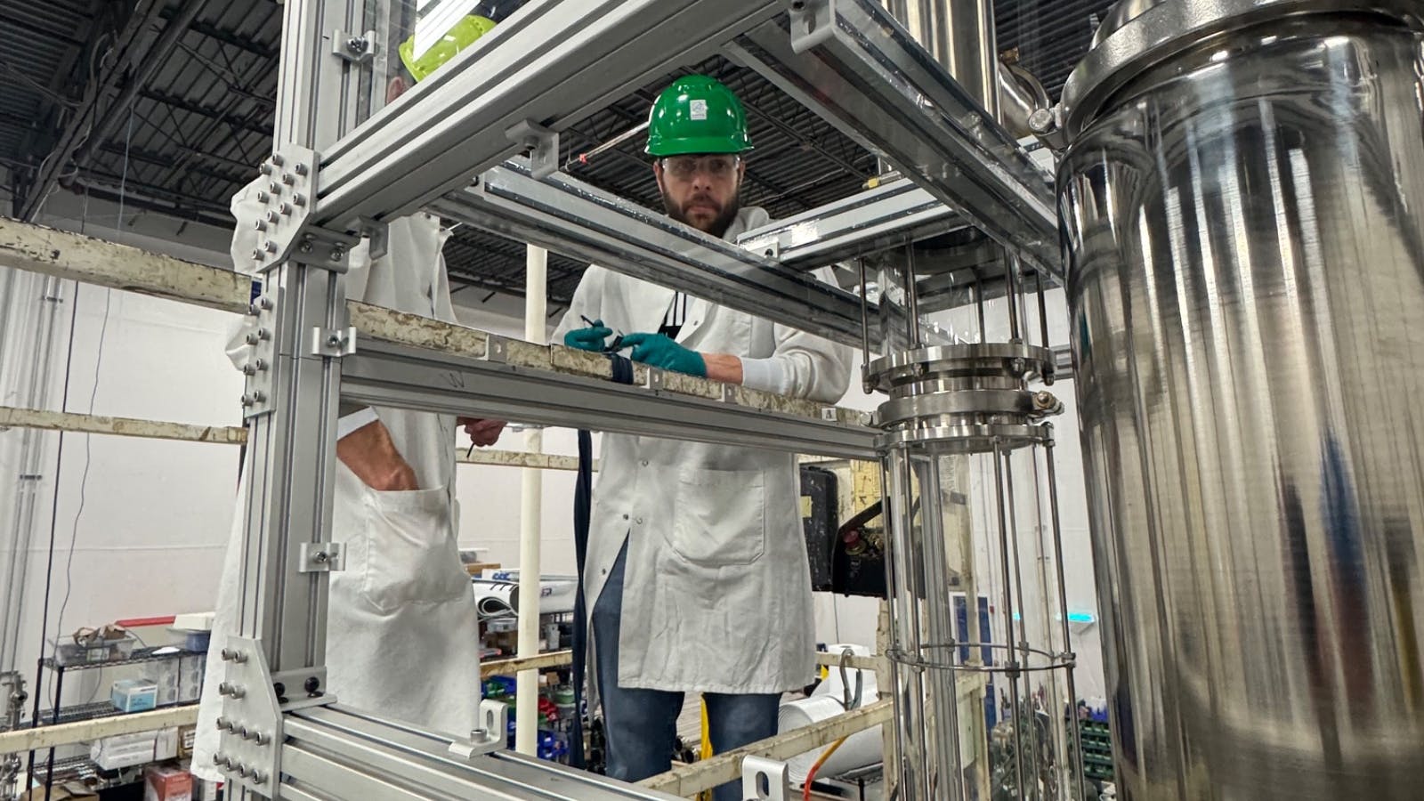 Worker in white lab coat and green hard hat inspects Capra modular bioreactor