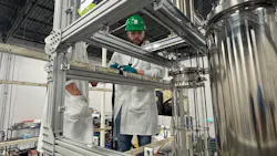 Worker in white lab coat and green hard hat inspects Capra modular bioreactor