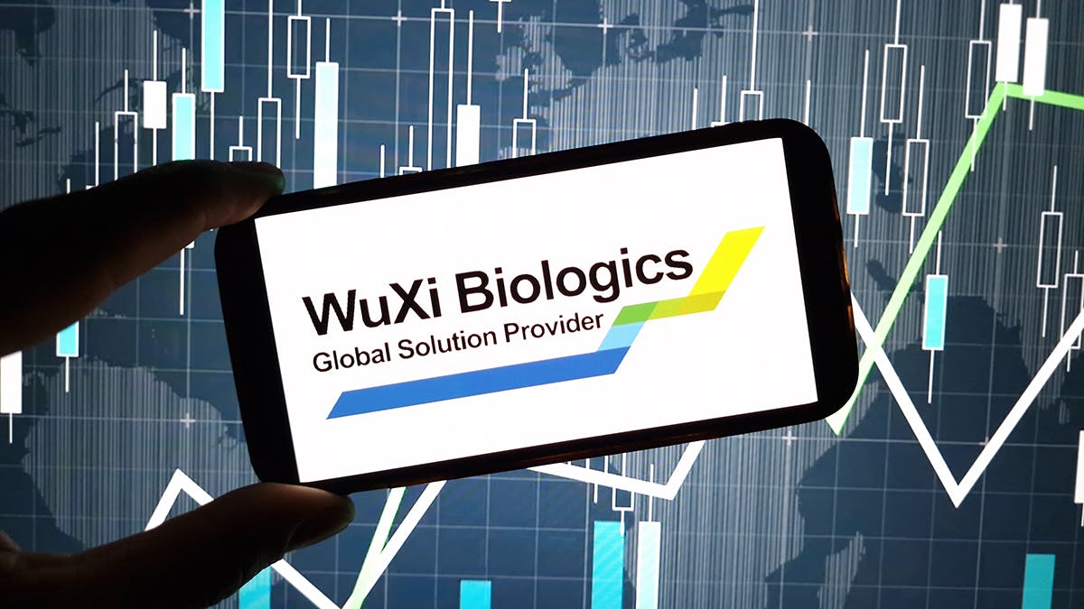 hand holds cell phone with WuXi Biologics logo on screen with digital graphics in background