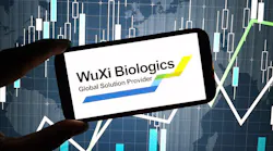 hand holds cell phone with WuXi Biologics logo on screen with digital graphics in background