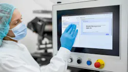 Pharmceutical work in blue mask and gloves stands in front of control panel for manufacturing execution system