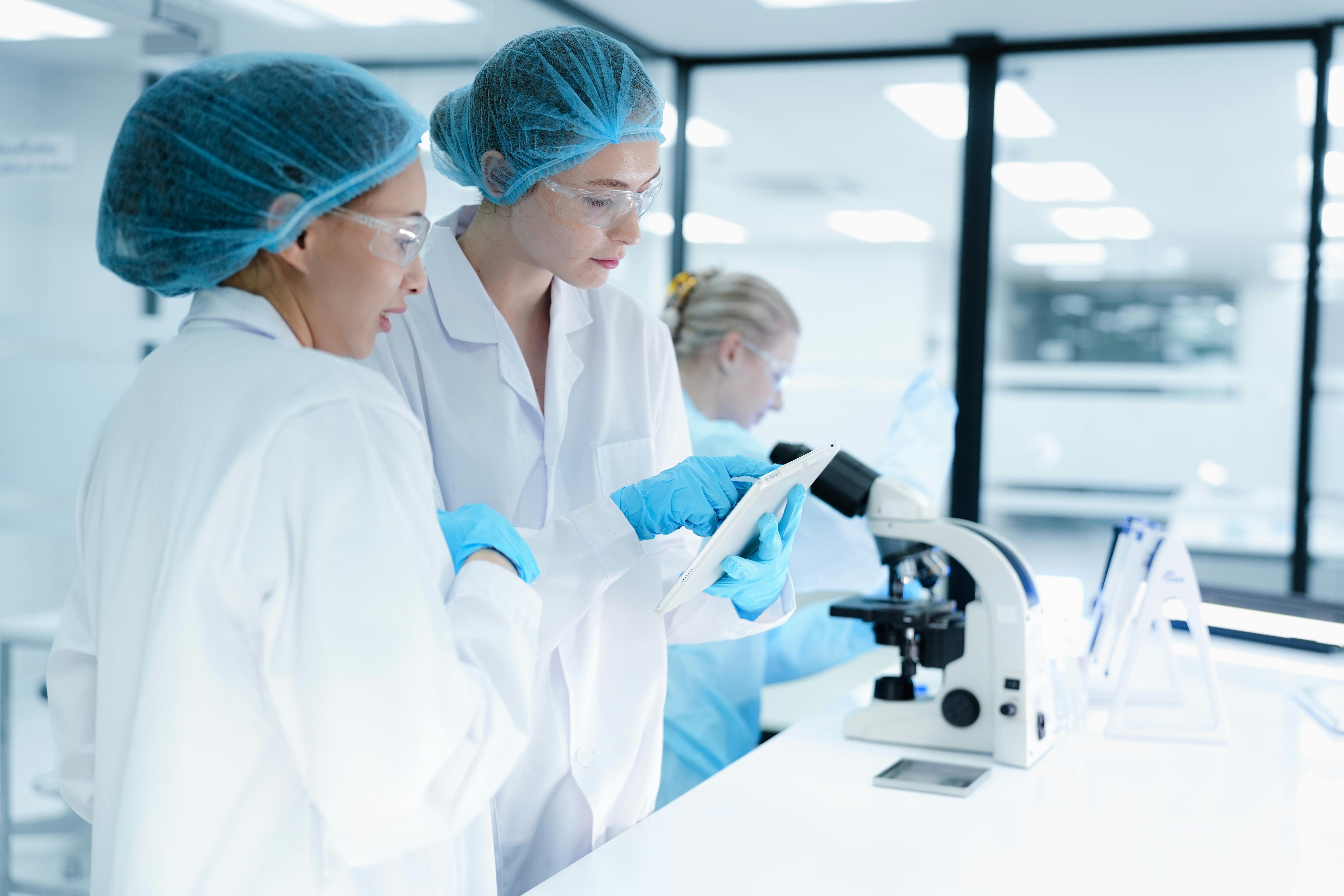 A pharmaceutical Quality Control QC team ensures GxP compliance. Two scientists review an electronic batch record on a tablet while a third performs a required analytical test.