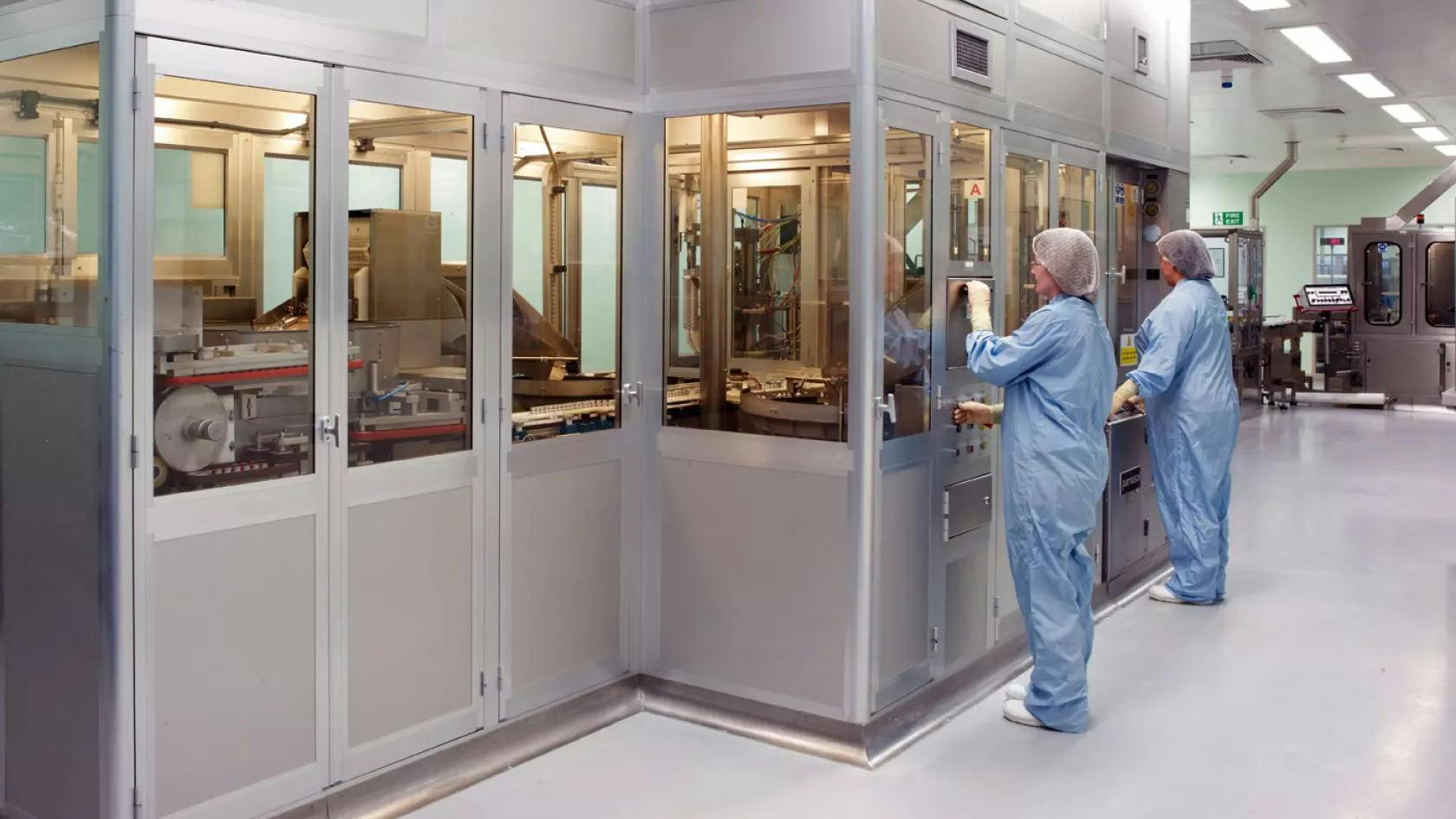 Two workers in PPE stand in front of pharma operations enclosure at Bespak facility in Holmes Chapel, UK