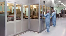 Two workers in PPE stand in front of pharma operations enclosure at Bespak facility in Holmes Chapel, UK