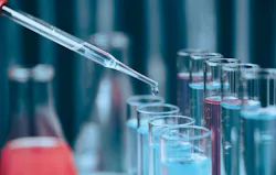 Laboratory pipette dispensing a liquid droplet above glass test tubes containing blue and pink solutions, representing chemical analysis, laboratory research and scientific testing.